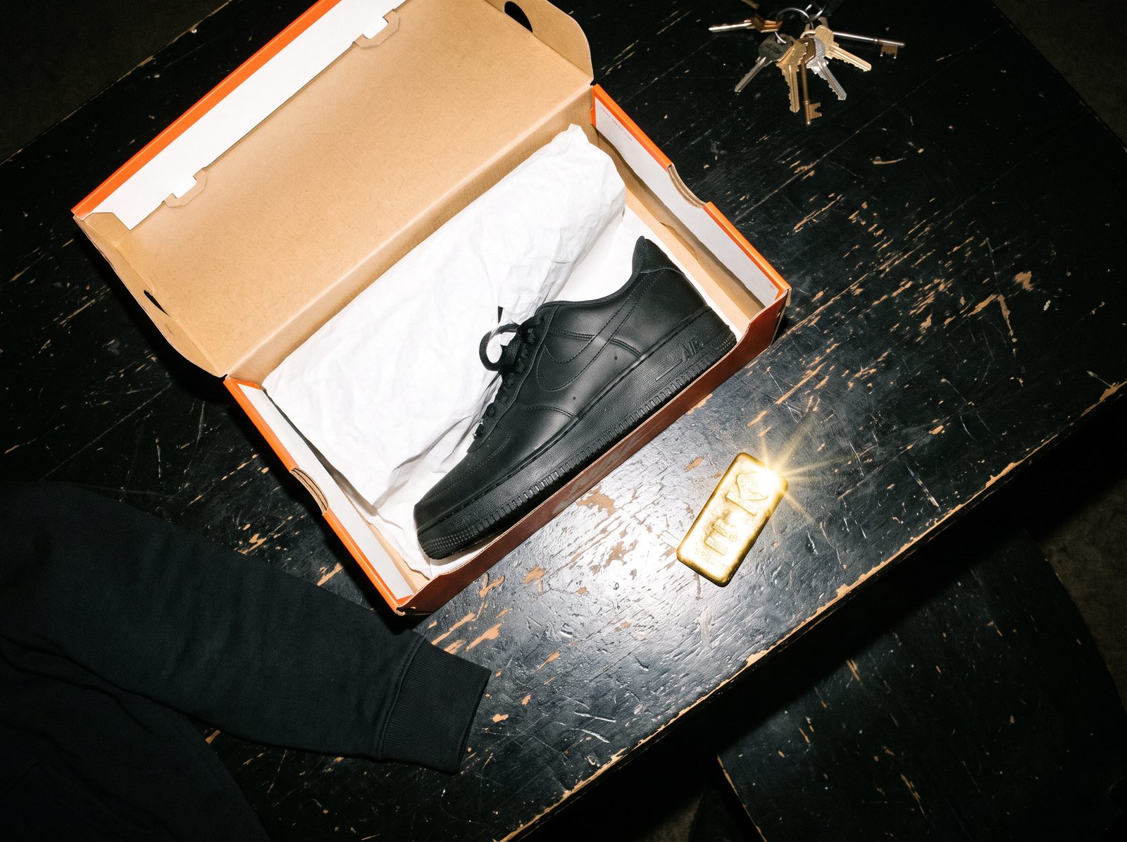 Open shoebox with a black Air Force 1 next to a gold bar