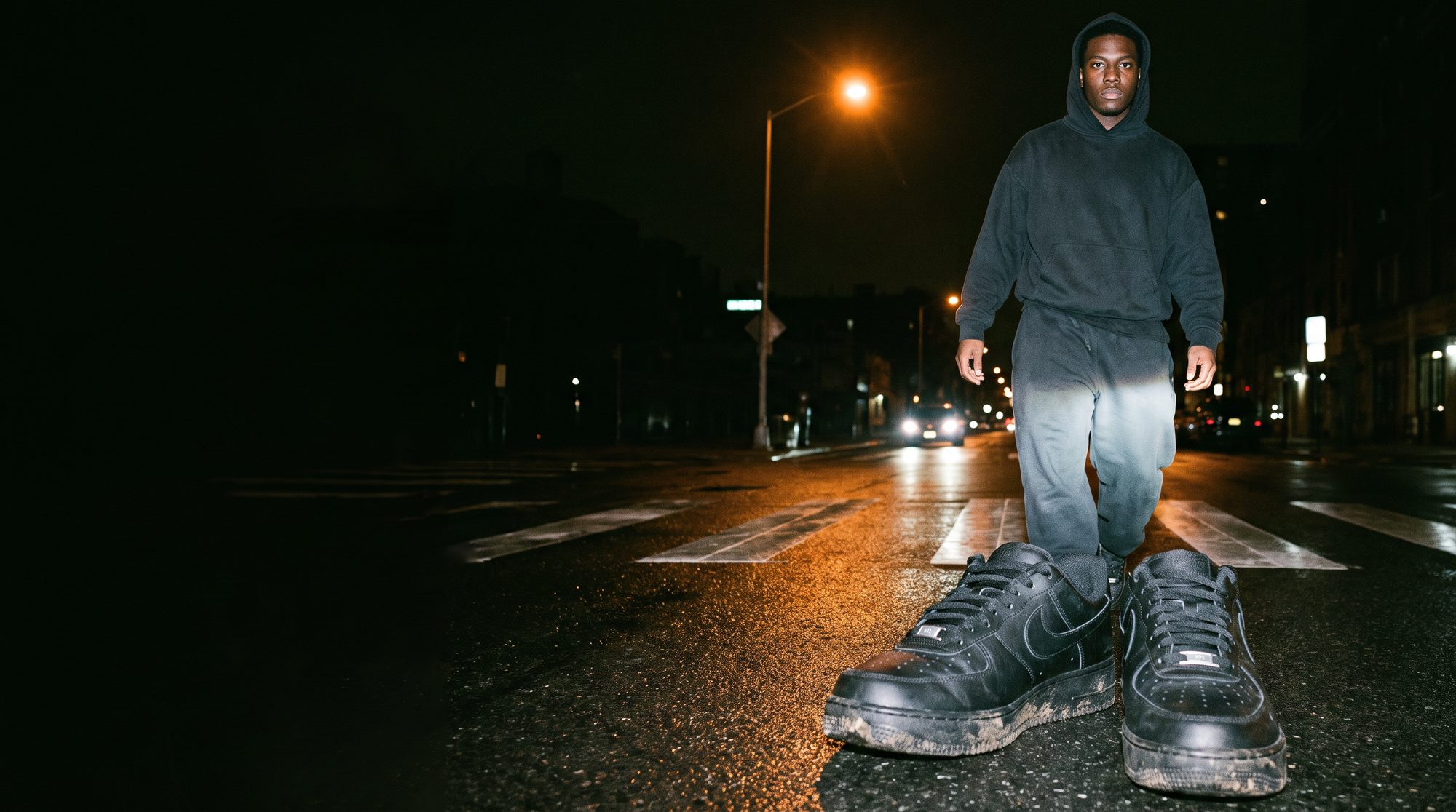 Man in a black hoodie crossing the street at night in black Air Force 1s